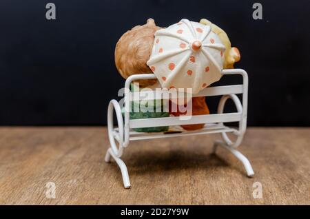 Ceramic figurines of children with an umbrella on a bench with their backs to the camera on a wooden background Stock Photo