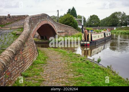 A narrowboat making the sharp turn onto the Trent and Mersey canal under the bridge at Great Haywood Stock Photo