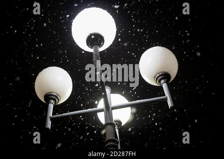 Street white round lantern at night during snowfall close-up, bottom view Stock Photo