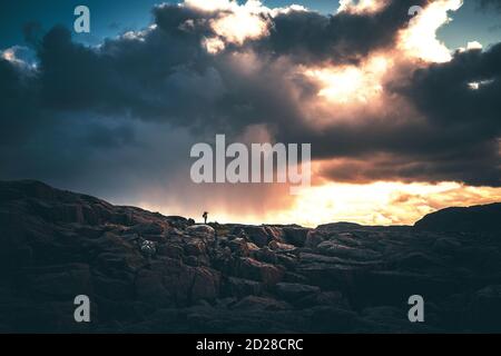 Man from behind with a backpack is trekking along a mountain trail in dense fog against the background of a gray cloud. Active lifestyle. Selected focus Stock Photo