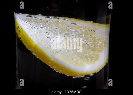 a glass of fresh drinking water and lemon on black background. bubbles in a glass mineral water as a thirst quencher. Stock Photo