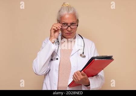 Senior female doctor with folders looking at camera through glasses. Stock Photo