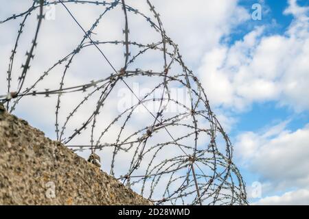 Stone fence with barbed wire on blue sky background with clouds close up Stock Photo