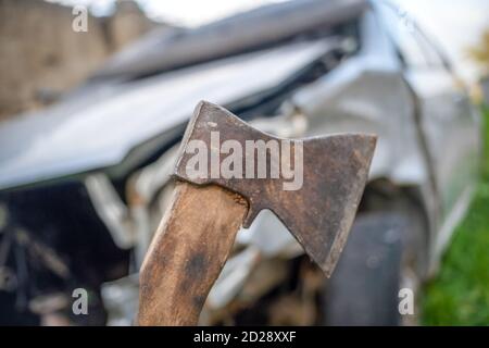 Hand of a man with an axe close - up on the background of a broken car Stock Photo