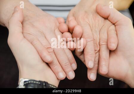 Hands of a young man holding the hands of an old, elderly woman close-up Stock Photo