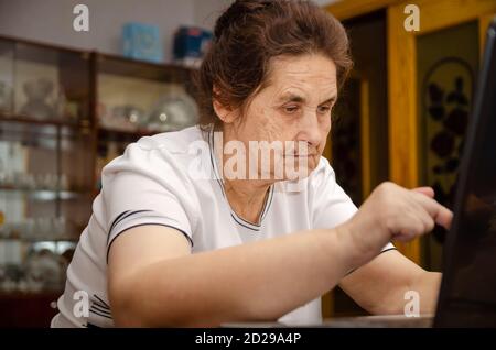 elderly dark-haired woman is sitting at a Desk typing on a laptop Stock Photo