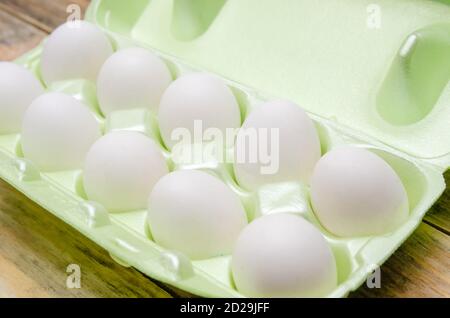 White eggs in green plastic packaging on a wooden background close up Stock Photo