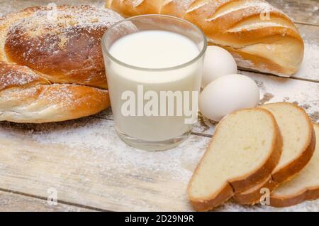 glass of milk, loaf, two eggs on a wooden background with flour Stock Photo