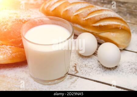 glass of milk, loaf, two eggs on a wooden background with flour Stock Photo