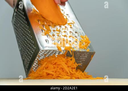 Women's hands grating juicy, delicious carrot on a grater close-up Stock Photo