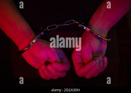 man in handcuffs, hands behind his back in the light of the lights of a police car Stock Photo