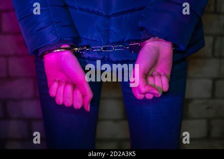 Woman in handcuffs, hands behind his back in the light of the lights of a police car Stock Photo