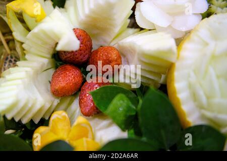 Carving with vegetables and fruits-strawberries and melon in the form of a flower on the holiday table. Stock Photo