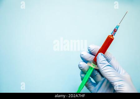 hand in blue gloves holds a syringe with blood or vaccine on a blue background with a copy of the space Stock Photo