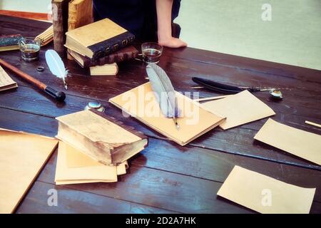 Table with vintage writing utensils. Books, paper and feather for writing in ink. Stock Photo