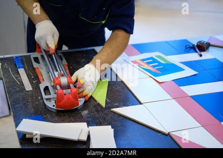 A man cuts a tile on a table to create a drawing from its pieces Stock Photo