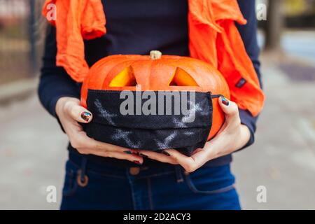 Halloween jack-o-lantern pumpkin in protective mask. Woman holds hand-made carved pumpkin outdoors. Coronavirus Stock Photo