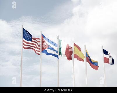 many colorful national flags of different countries on masts outdoor on blue cloudy sky background, symbols of usa cuba ireland spain venezuela and dominican republic Stock Photo