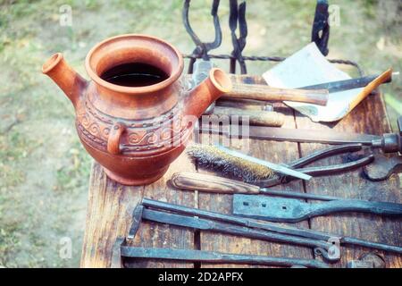 Retro blacksmith tools on wooden table in forge. Pitcher for hardening iron, tongs and other tools for forging. Stock Photo