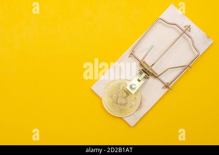 mousetrap with a gold bitcoin on a yellow background. Risks and dangers of investing in bitcoin, concept Stock Photo