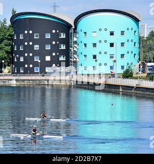 Two rowers prepare for sculling training session on rowing course at Royal Albert Dock UEL campus buildings reflections Newham East London UK Stock Photo