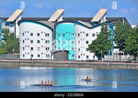 Royal Docks rowing course young women athletes training coxless quadruple scull & two young men rowers in double scull UEL campus buildings beyond UK Stock Photo