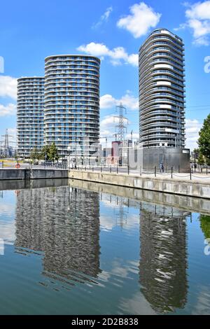 Reflections in the Royal Docks water of modern high rise housing apartment block structures of homes in flats with balconies Newham East London UK Stock Photo