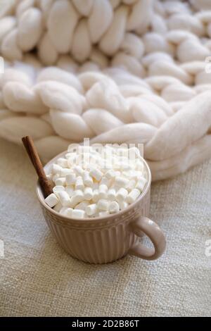 Close up of winter hot drink. Cocoa with marshmallows in a cup is on the bed on a knitted blanket. The concept of coziness and holidays Stock Photo