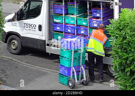 Tesco supermarket home delivery van open side of groceries in food crates & driver worker unloading online grocery shopping onto trolley  England UK Stock Photo