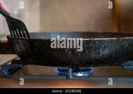 Old frying pan stands on the stove with the gas turned on close-up. Cooking food at home. Stock Photo