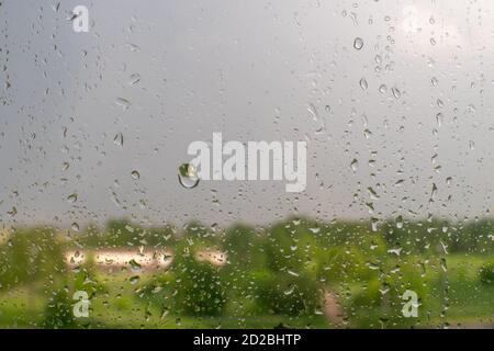 Raindrops on a window with green trees and a cloudy sky in the background on a summer day Stock Photo