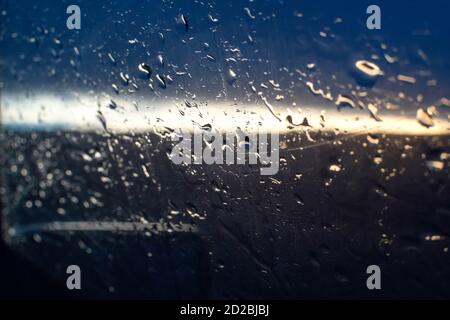 Raindrops on the side window of the car against the background of the sunset and the silhouette of a tree, a photo from inside the car Stock Photo
