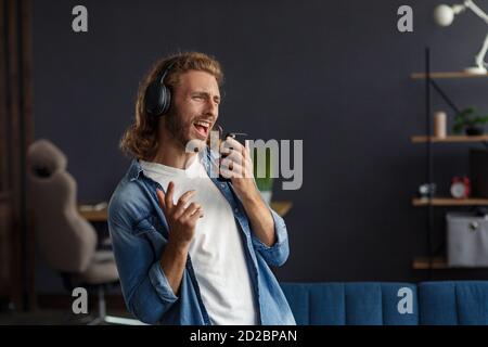 Handsome long haired curly man with headphones listening music,singing and dancing.Funny emotional smiling man with earphones and mobile phone relax Stock Photo