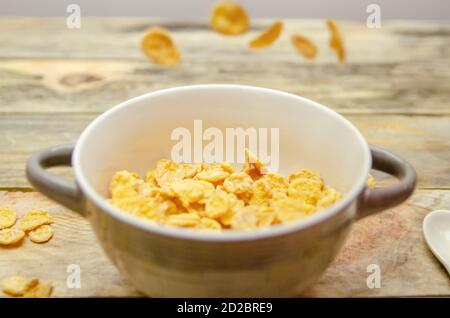 Bowl with falling corn flakes on a wooden background Stock Photo