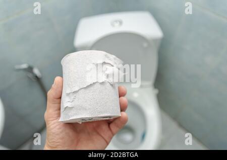 A man's hand holds a roll of white toilet paper over the toilet close-up Stock Photo