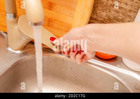 womens brown hand opens the tap in the kitchen close-up, flowing water from the faucet; focus on the arm and crane Stock Photo