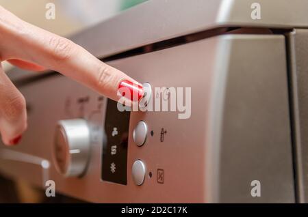 Female hand with red nail polish presses the button to adjust the time in the dishwasher Stock Photo