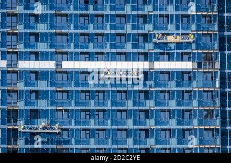 Construction of a large residential complex of glass on a Sunny day. Three hanging construction cradles. Construction concept. Georgia, Batumi Stock Photo