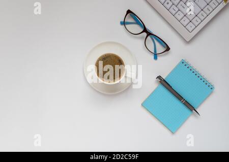 Computer keyboard, a cap of coffee, glasses, notepad and pen on a white surface. Stock Photo