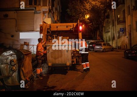 Tbilisi, Georgia - June 27 2019: Two workers in the orange garbage collection uniform loading garbage into the garbage truck at night Stock Photo