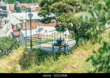 Rear view of a man and a woman on a bench on a sunny day under a tree. Contemplative and desirable mood. Stock Photo