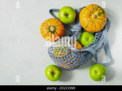 Small ripe pumpkins and green apples in an ecological string bag. Stock Photo