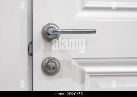Metal handle with a rotary lock on a white half-open door, close-up. The element door in the style of French Provence Stock Photo