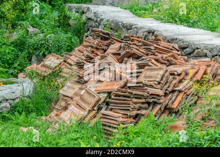 A big pile of old brown roof tiles lay on the grass on a sunny day. Stock Photo