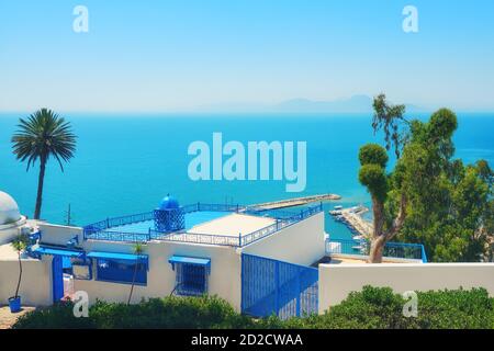 Sea view and arabic cafe with palm tree in Sidi Bou Said. House white and blue color - Sidi Bou Said, Tunisia, 06 18 2019 Stock Photo