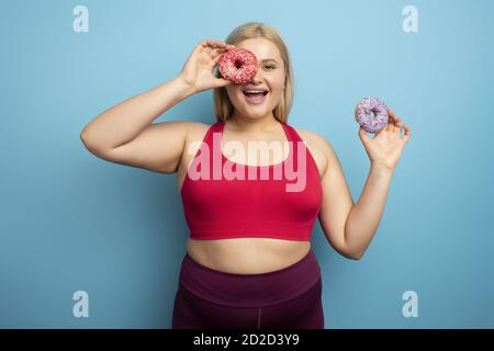 Fat woman eats sweet instead of do gym. Cyan background Stock Photo