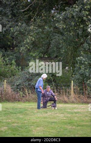 Dog Training class. Owner holding a Border Collie on a longer lead whilst Instructor on her knee, gives advice on gaining the animals attention. Stock Photo