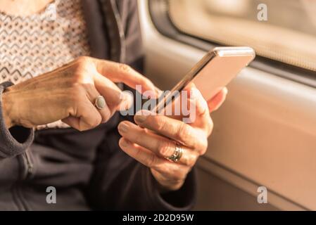 Adult woman's hands approaching writing a text on the mobile in the train Stock Photo