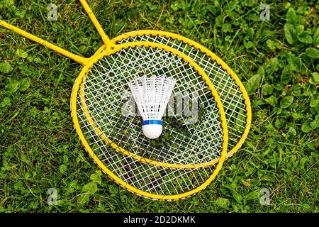 white shuttlecock close-up on yellow badminton rackets in the green grass, top down view Stock Photo
