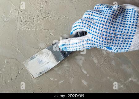 Close ap hand in work glove holds construction spatula and covers the surface with plaster Stock Photo